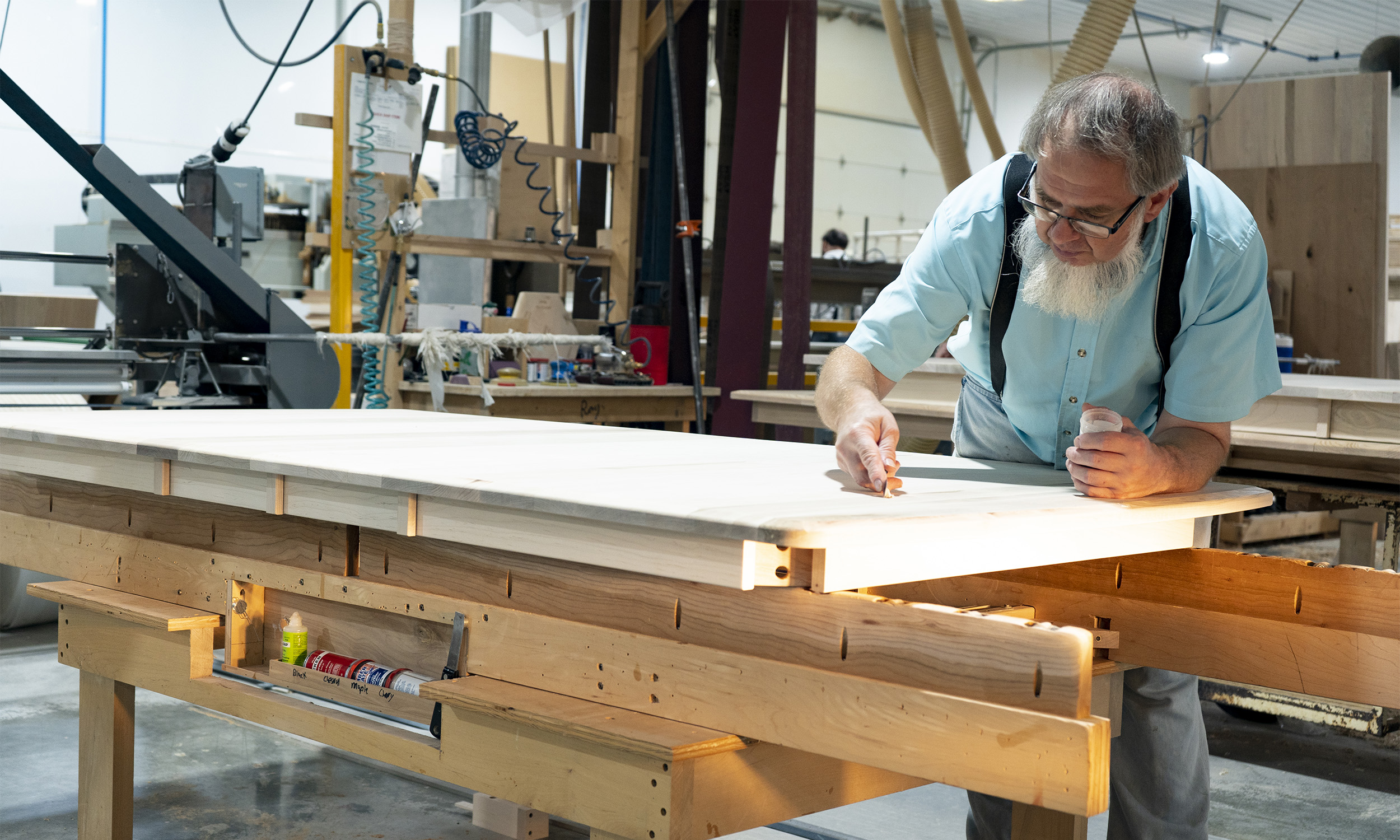 Amish craftsman hand-finishing a solid wood furniture panel in woodworking shop