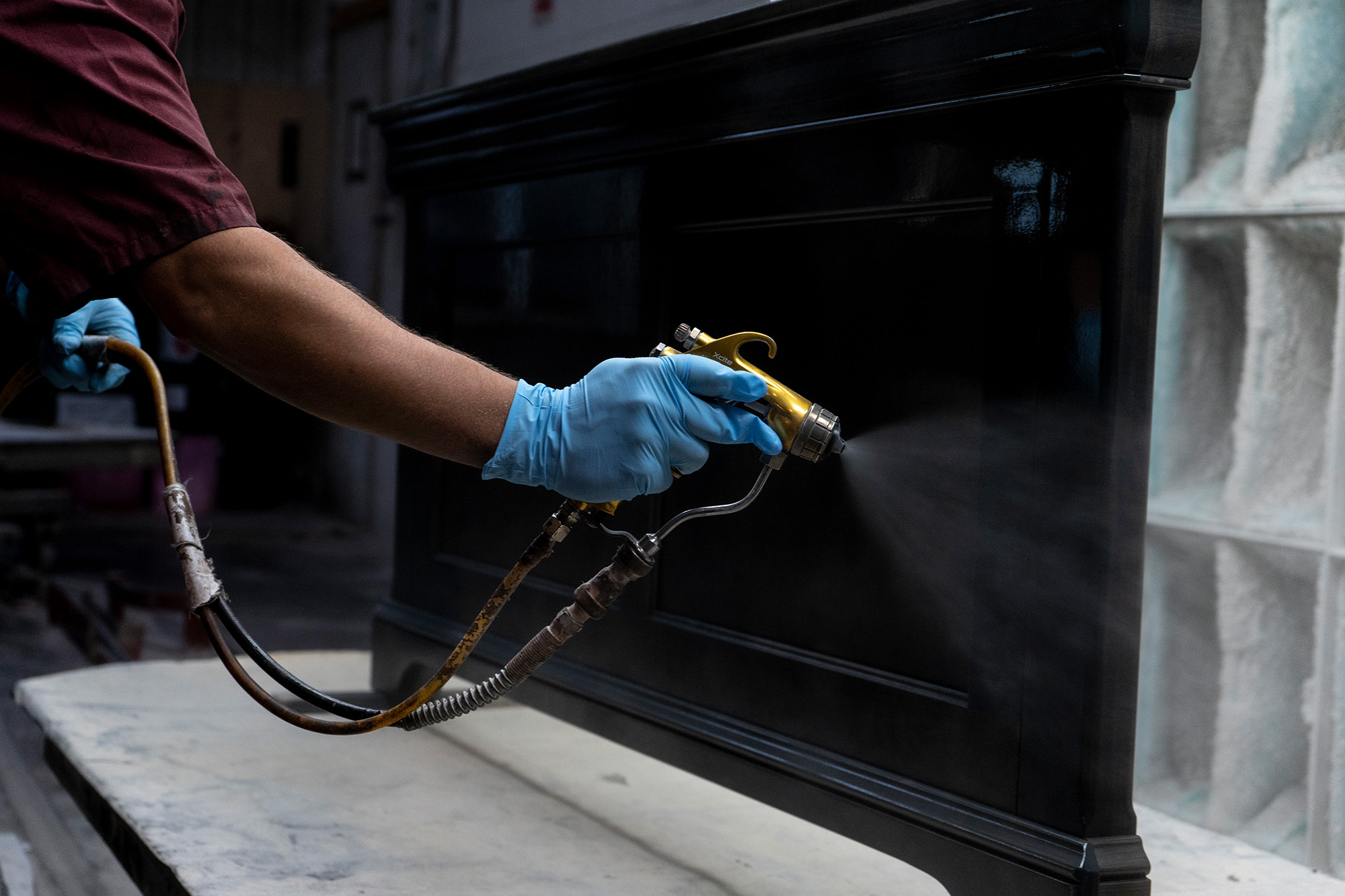Spray finishing a black solid wood furniture headboard in a workshop